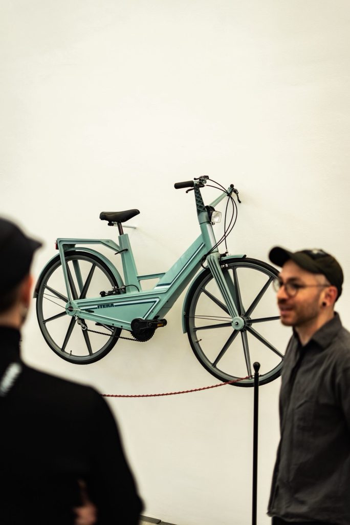 A mint green bicycle mounted on a wall, with two people standing in front of it in a gallery setting.