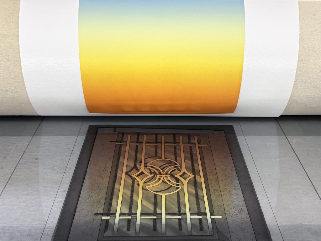 A close-up of a rolled piece of paper featuring a gradient design transitioning from blue to yellow, placed above a dark, intricate geometric pattern on a flat surface.