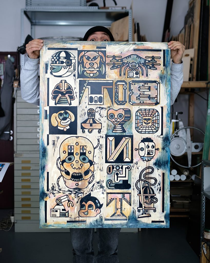 A person holding a large, colorful artwork featuring various abstract designs and characters, standing in a studio environment.