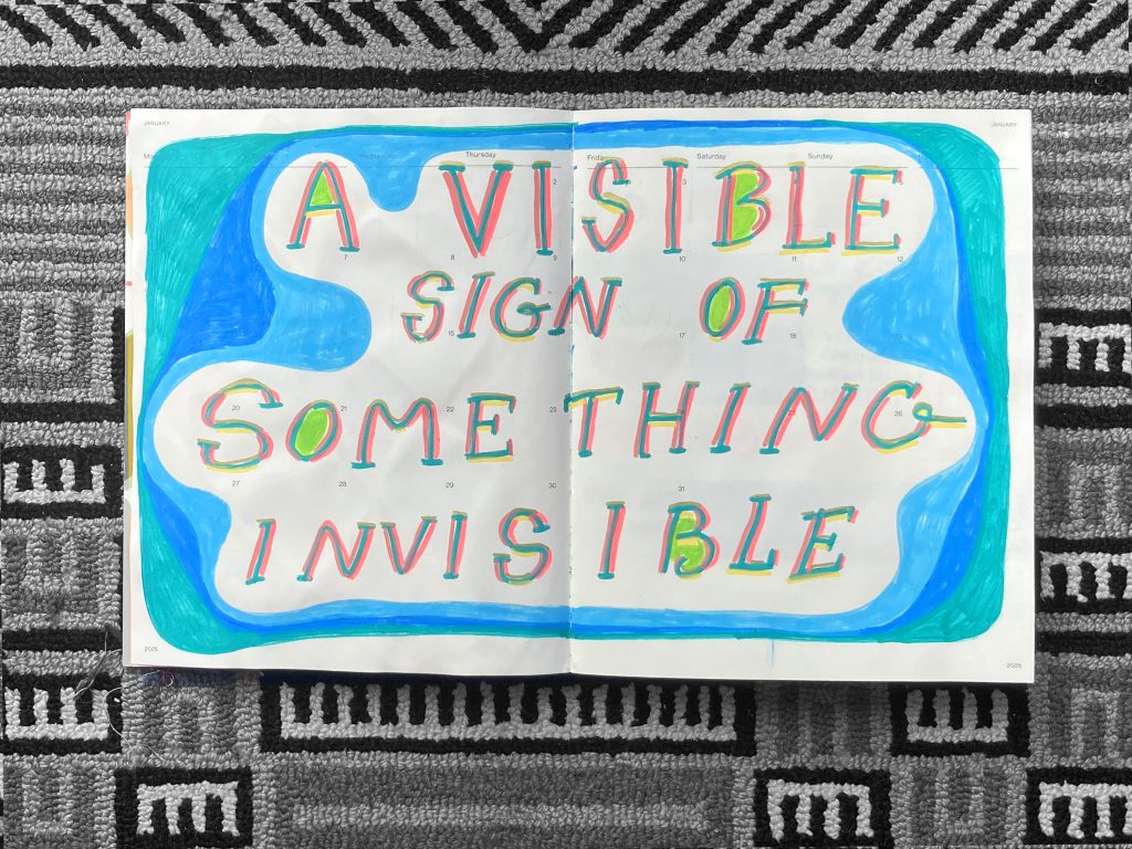 Open sketchbook page featuring the colorful handwritten phrase 'A VISIBLE SIGN OF SOMETHING INVISIBLE' against a backdrop of blue and green shapes, placed on a textured black and white patterned rug.
