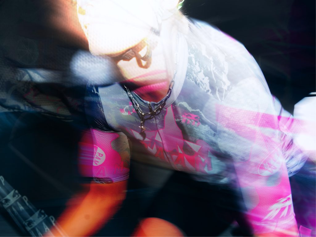 A blurred action shot of a cyclist in vibrant, colorful attire, featuring dynamic movement and a sense of speed.