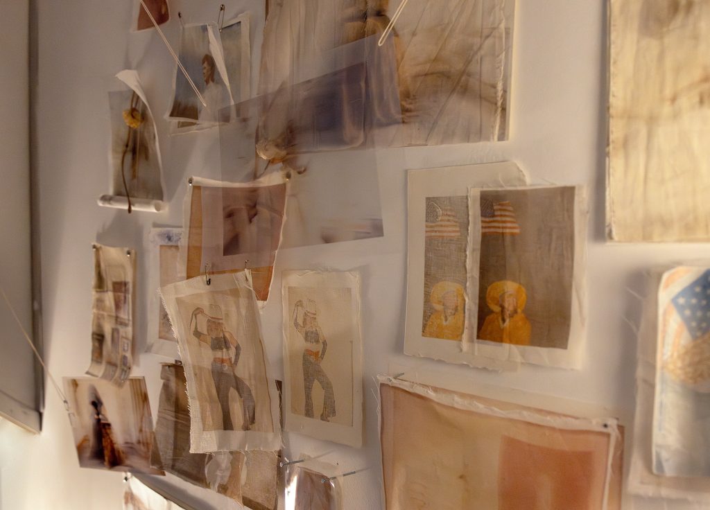 A collection of various photographs displayed on a wall, featuring faded images and artistic elements, some held with clips or hanging loosely.