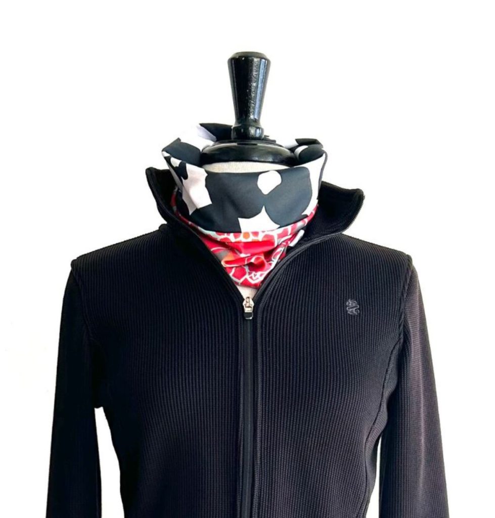 A black zip-up jacket displayed on a mannequin, featuring a colorful patterned scarf around the neck.