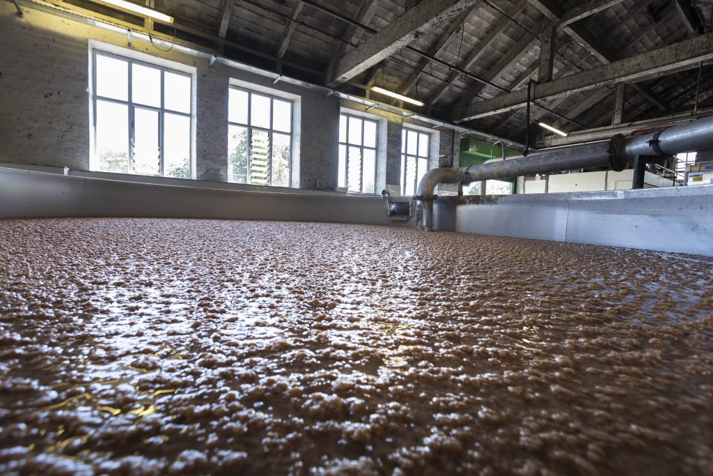 Interior of a industrial facility with large tanks filled with a brown, bubbling liquid, under natural light from large windows.