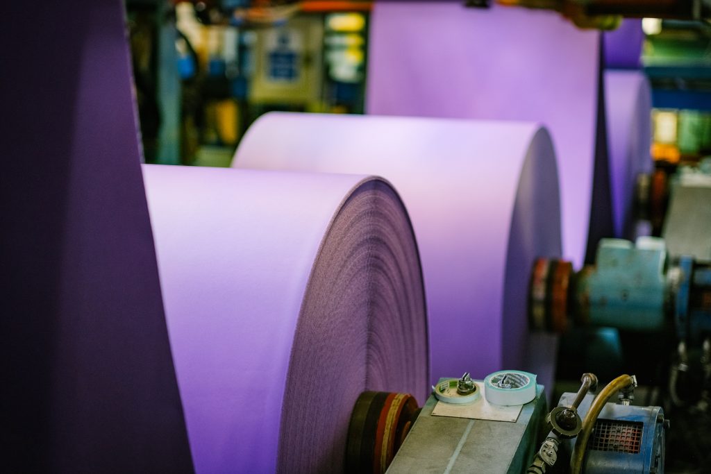 Close-up of large rolls of purple paper being processed in an industrial setting.