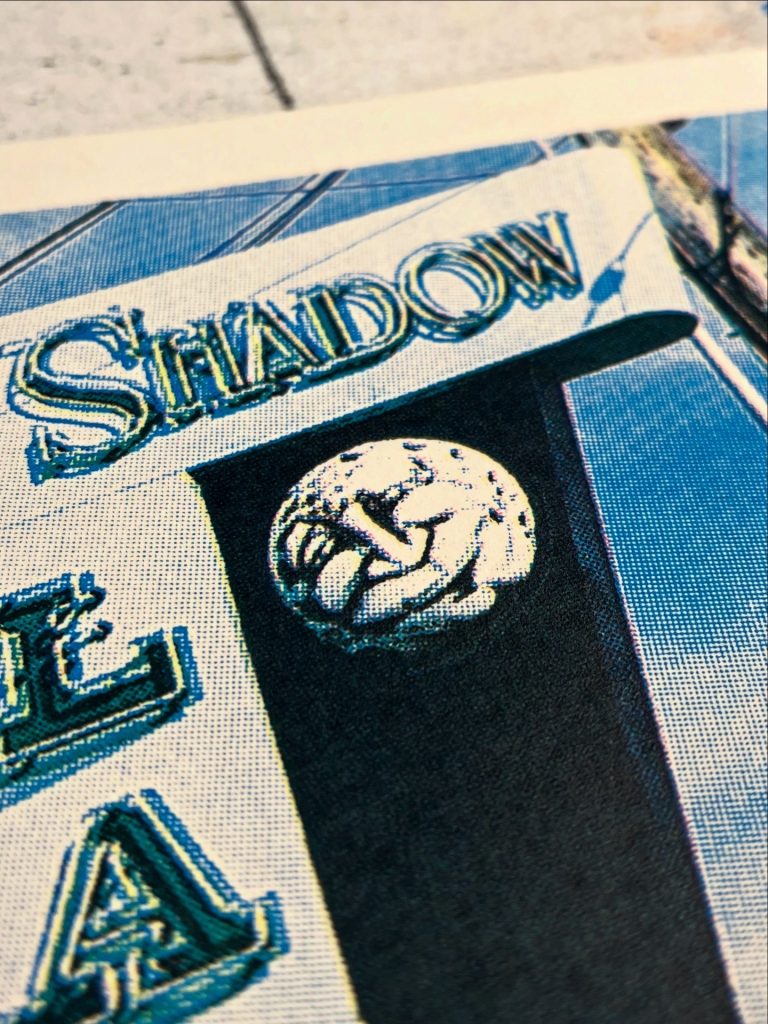 Close-up of a sign featuring the word 'Shadow' and a decorative circular emblem with intertwined figures.