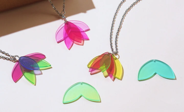 Colorful layered flower-shaped pendants in pink, green, yellow, and blue on silver chains, with additional matching pieces in various colors.