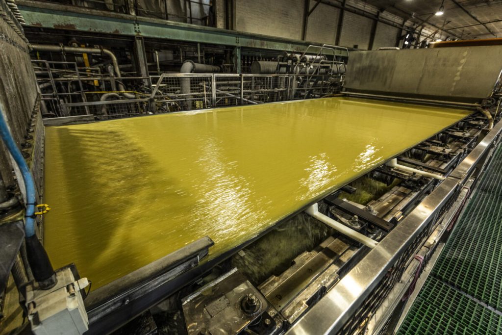 Large industrial tank filled with a yellow liquid, reflecting light, surrounded by machinery in a factory setting.