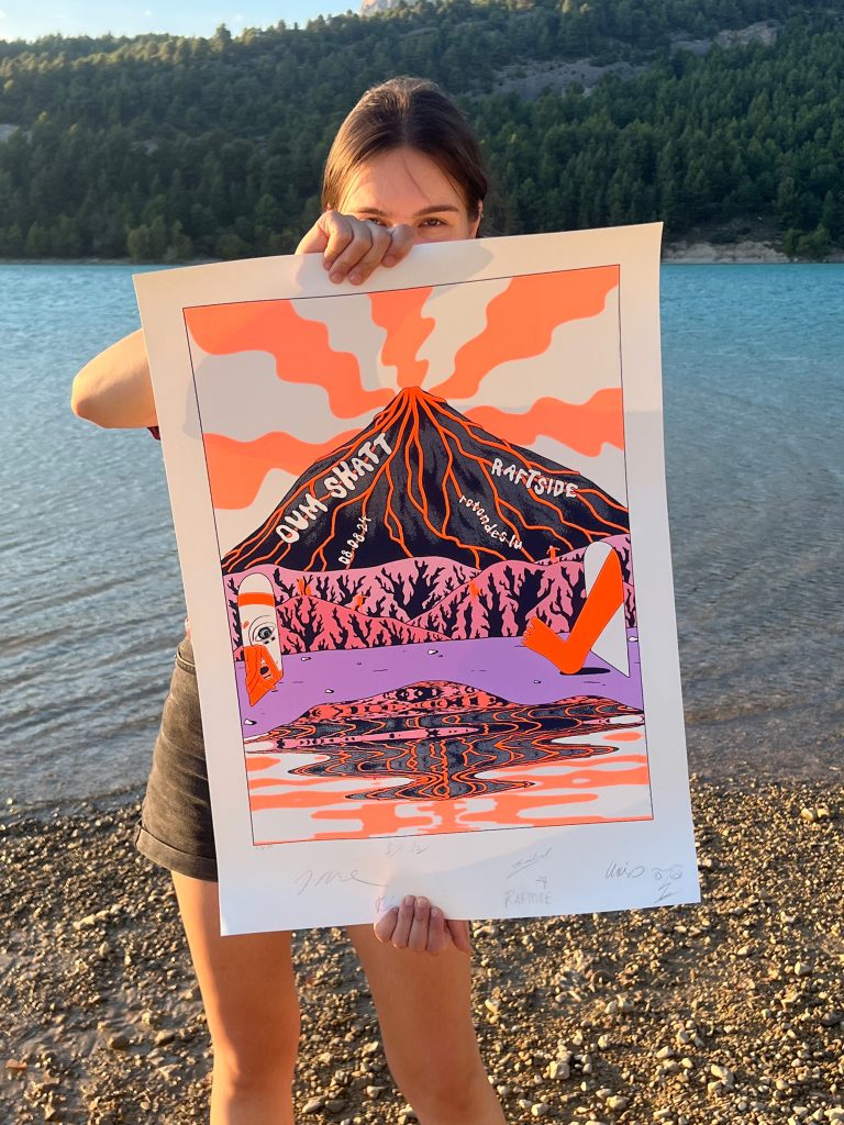 A person holding a colorful art print depicting a stylized mountain, surrounded by trees and a reflective water surface, with vibrant orange, pink, and purple hues.