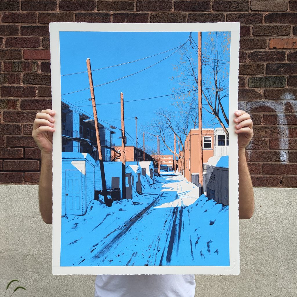 A person holding a large art print depicting a snowy alleyway with blue sky, telephone poles, and buildings.