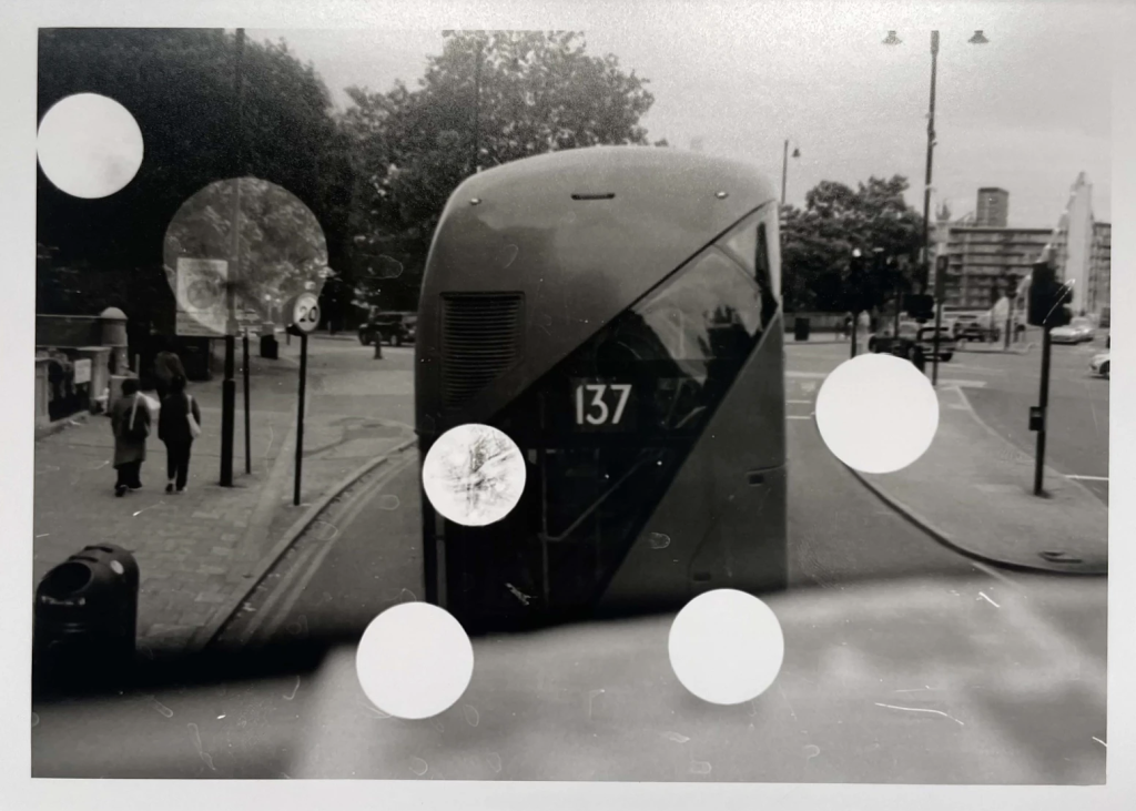 Black and white image of a bus displaying the number 137, taken from behind, with two people walking on the sidewalk and various circular overlays.