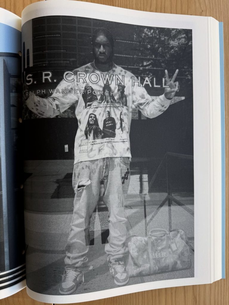 A black and white photograph of a person standing in front of S.R. Crown Hall, wearing a graphic sweatshirt and baggy jeans, with a peace sign gesture.