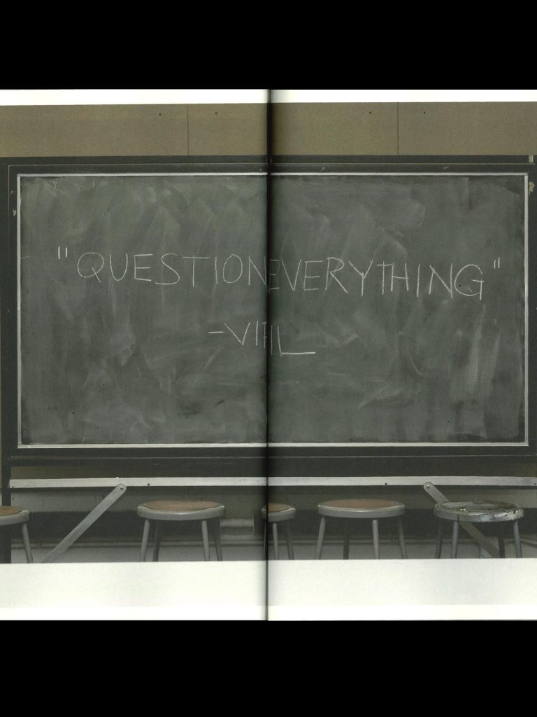 A chalkboard displaying the quote 'QUESTION EVERYTHING' attributed to VHL, with several empty stools in front of it.