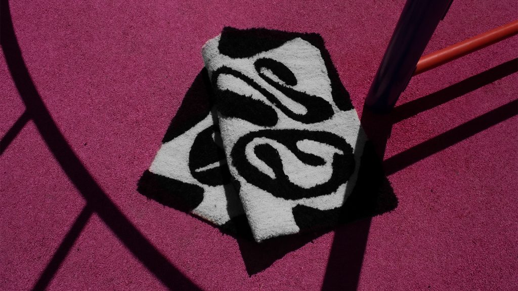 Two decorative rugs with a black and white abstract pattern on a vibrant pink surface.