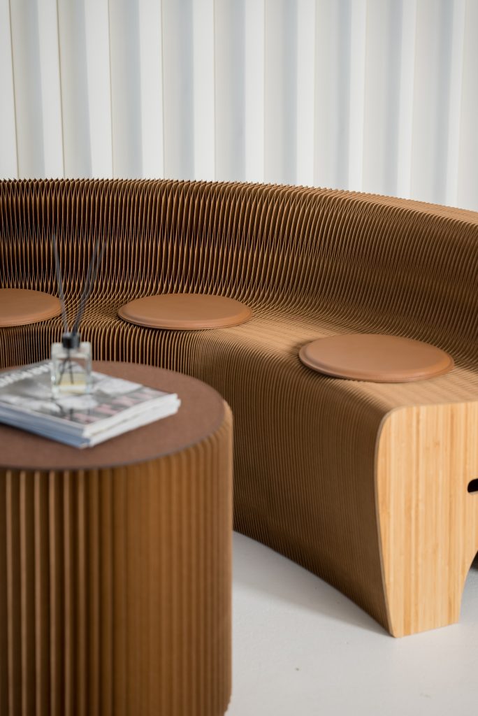 A modern curved wooden bench with circular leather cushions and a matching ribbed side table, set against a white background.